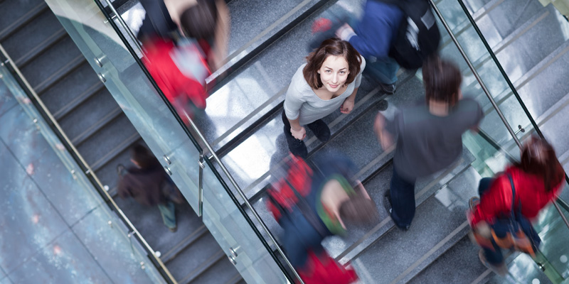 Student standing on stairs of university with others moving around her