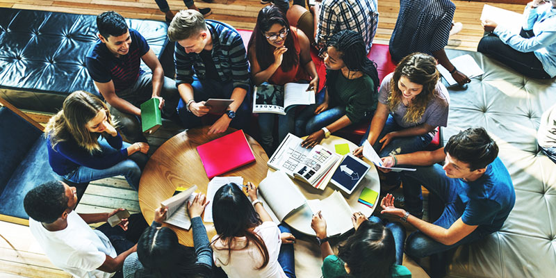 Large group of students around a coffee table with university work