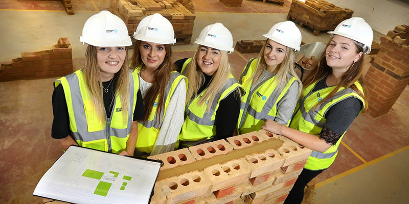 Five students on a construction site wearing high visibility jackets and hard hats