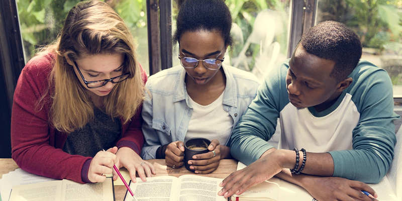 Three students working together looking at books