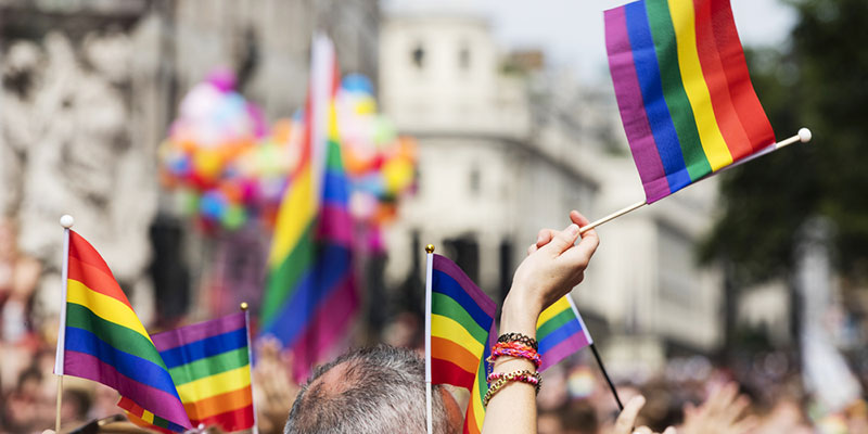 Pride rainbow flags being waved by a crowd