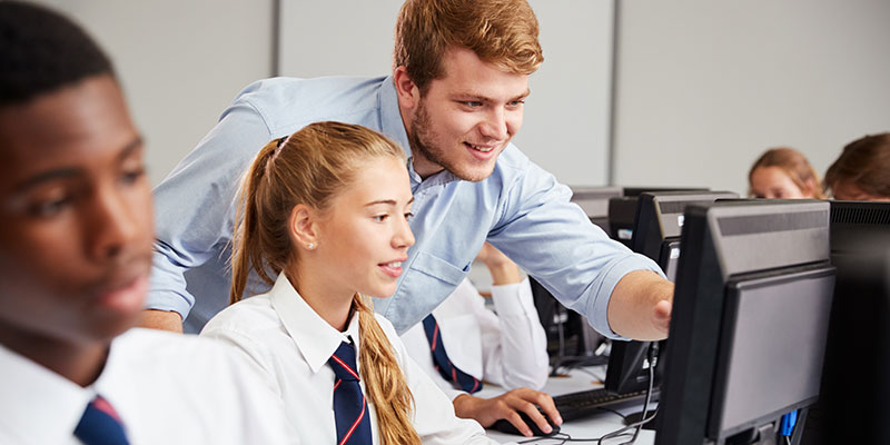Secondary school pupils working on computers. A teacher is helping one student