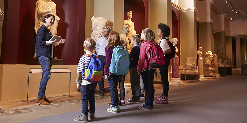 Primary school pupils are visiting a museum. A teacher is talking to them about the statues in the room.