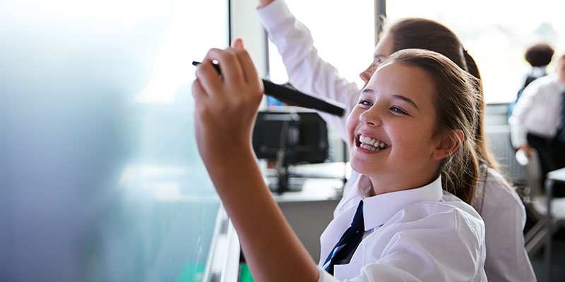 A secondary school pupil is smiling and writing on a whiteboard