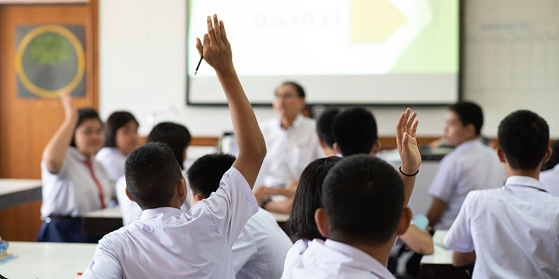 Classroom of secondary school pupils, three are raising their hands