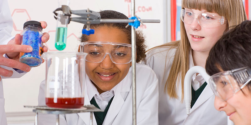 Three school pupils are observing a science experiment