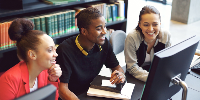 Three students working on a computer in the library