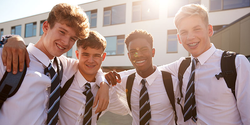 Group of four teenage school pupils in uniform, smiling