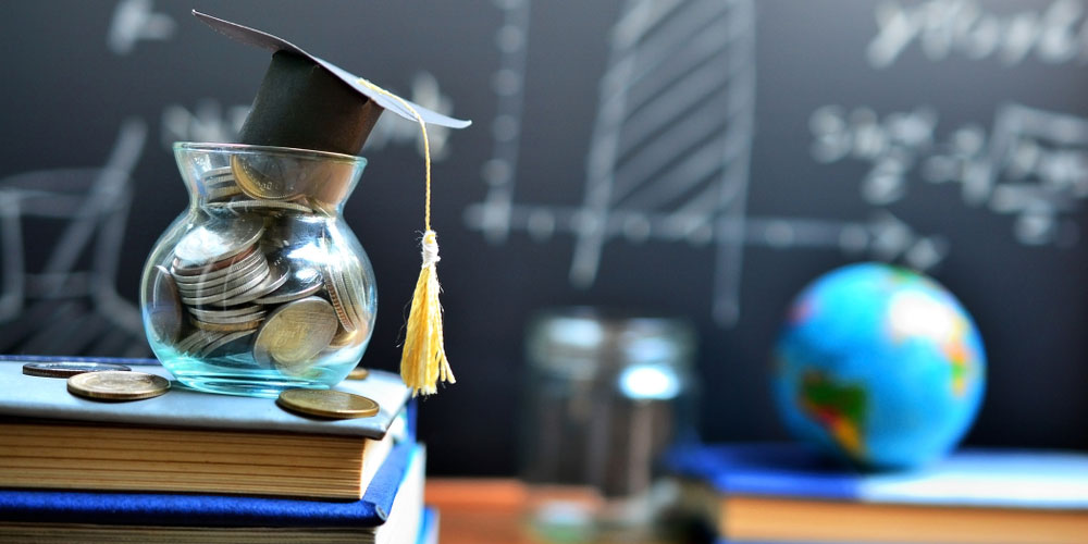 Coins in jar on text books on desk in front of blackboard - denoting money to fund education