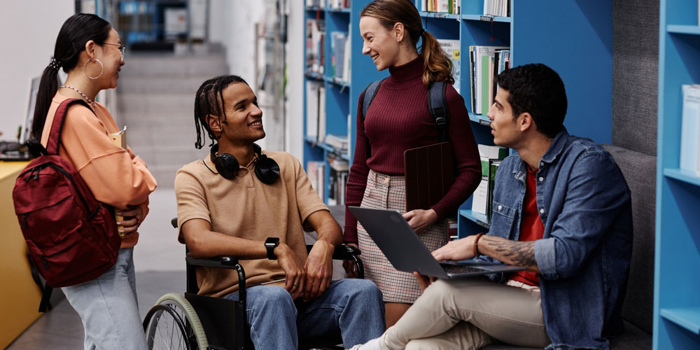 Small group of students chatting in a university library. One student is in a wheelchair.