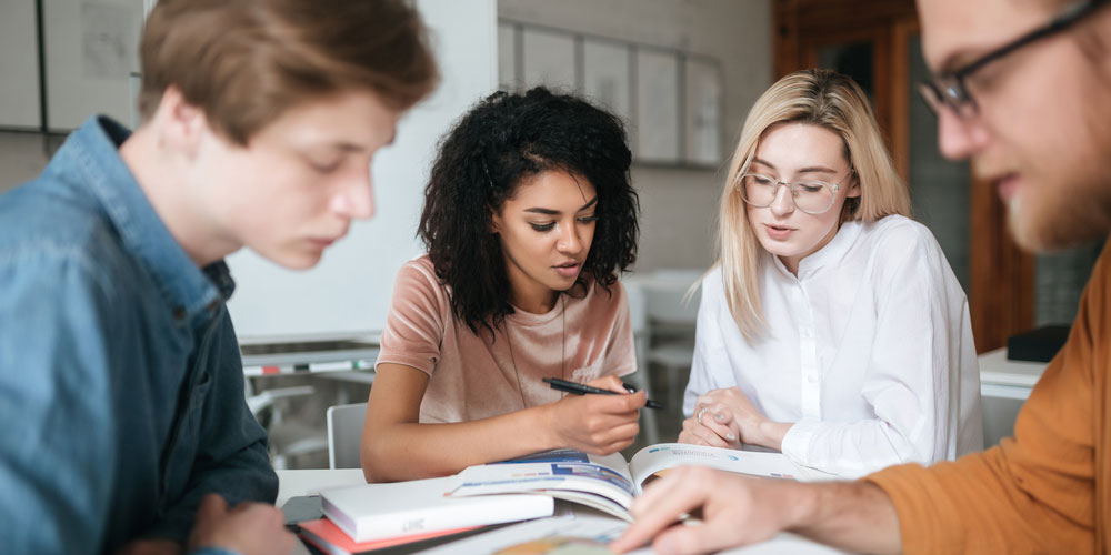 Two female and two male students studying at desk in classroom at university