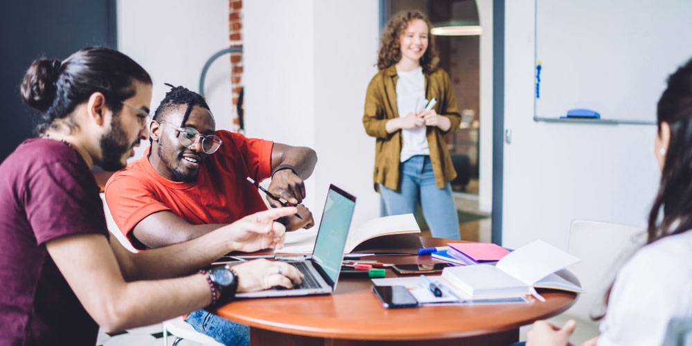 Four young graduates talking in business hub, two looking at laptop