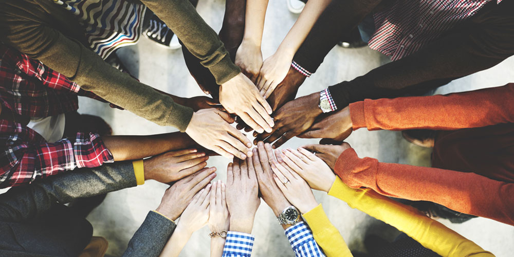 8 pairs of hands of different ethnicities touching in the middle of a circle