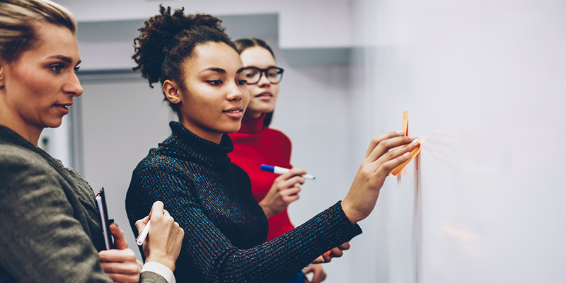 tutor watching student sticking note on whiteboard in university seminar