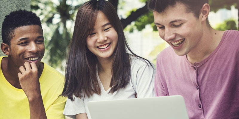 Three students outside looking at a laptop