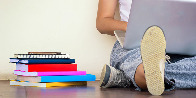 Student on laptop next to pile of books and notepads