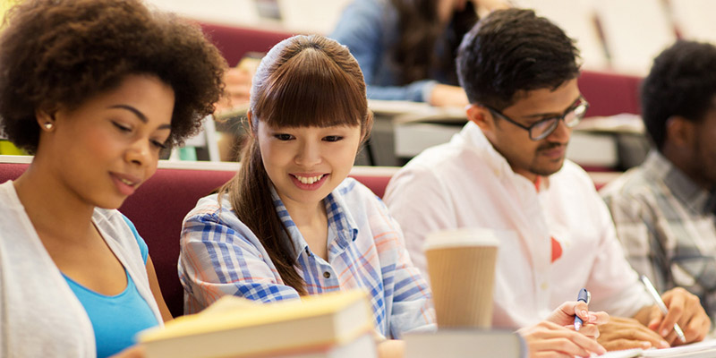 Three university students in a lecture theatre making notes