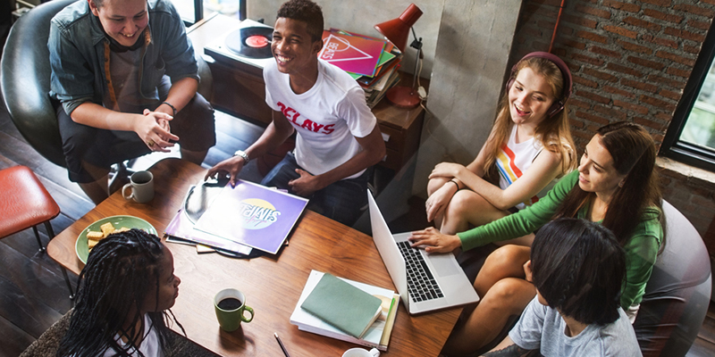 Group of six students sitting around a coffee table with laptop and books