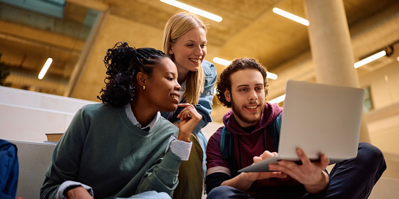Three higher education students looking at a laptop