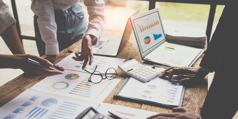 business people discussing financial figures around a desk with spreadsheets, charts and calculator.